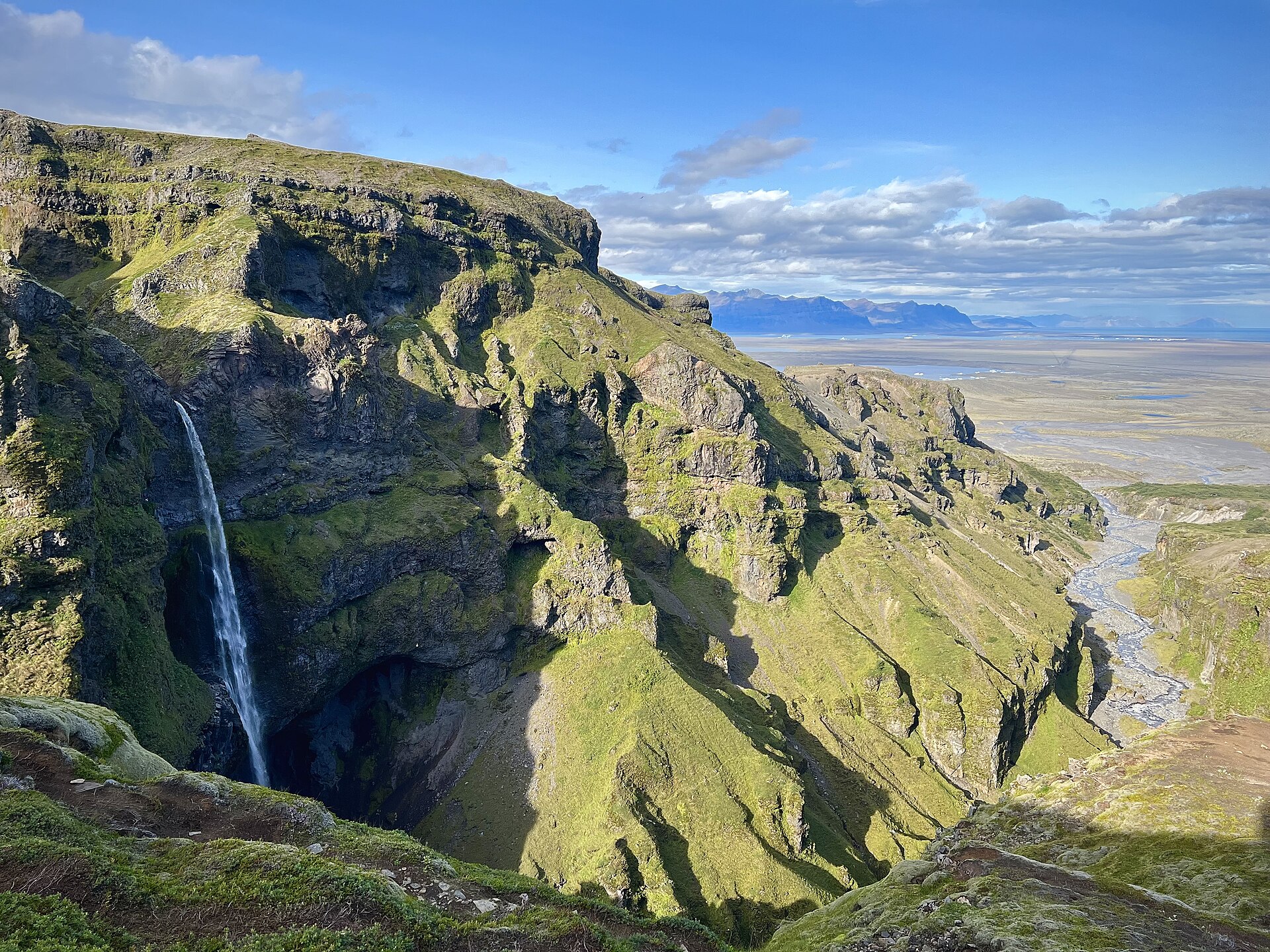 Múlagljúfur canyon mouth in sunshine, Hangandifoss falling into the gorge with the sandur and sea beyond